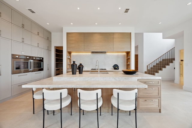 kitchen featuring oven, visible vents, a sink, a spacious island, and a breakfast bar area