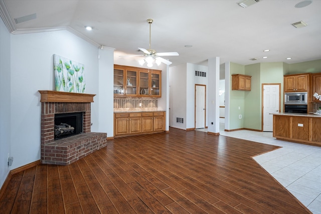 unfurnished living room featuring ornamental molding, ceiling fan, wood-type flooring, and a brick fireplace