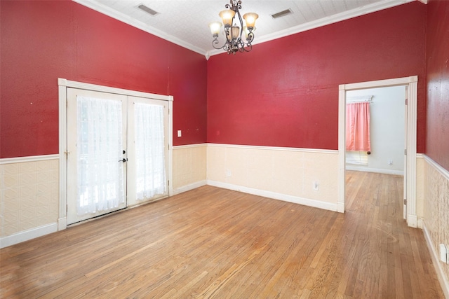 empty room featuring french doors, ornamental molding, a chandelier, and hardwood / wood-style floors