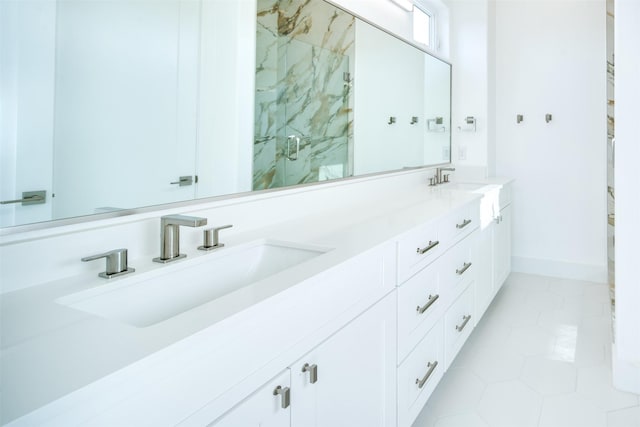full bath with double vanity, a sink, a marble finish shower, and baseboards