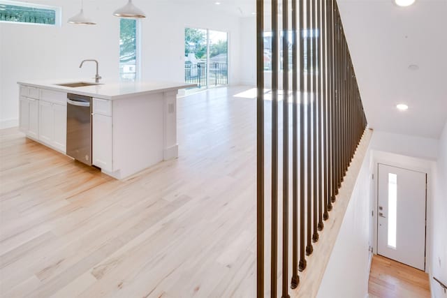 kitchen with decorative light fixtures, stainless steel dishwasher, white cabinetry, a sink, and light wood-style flooring