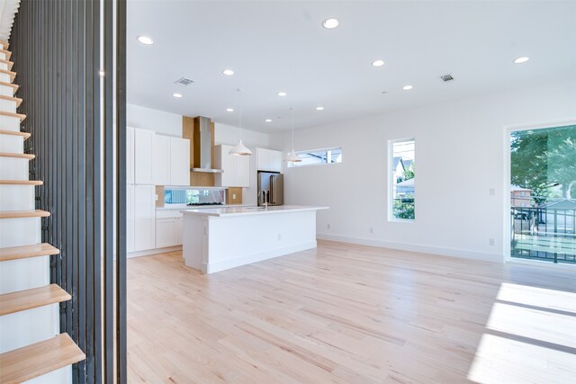 kitchen with wall chimney range hood, light hardwood / wood-style flooring, decorative light fixtures, high quality fridge, and white cabinetry