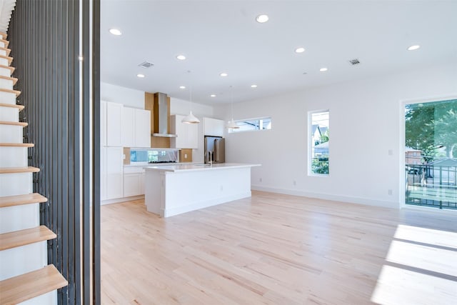 kitchen featuring light wood-style floors, freestanding refrigerator, wall chimney exhaust hood, and an island with sink