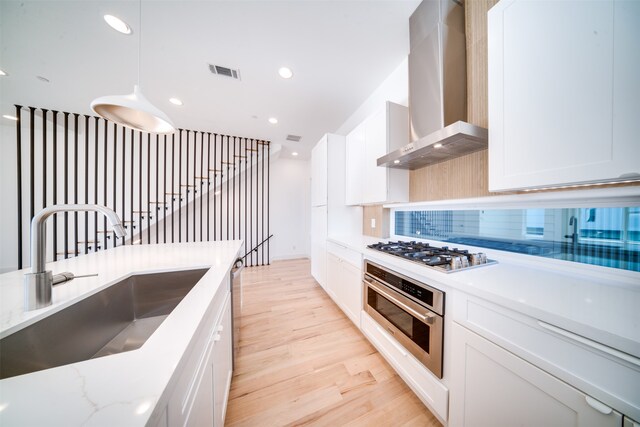 kitchen with appliances with stainless steel finishes, wall chimney range hood, white cabinetry, and light wood-type flooring