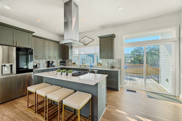 kitchen with sink, a kitchen island, island range hood, light hardwood / wood-style floors, and decorative backsplash