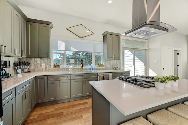 kitchen with tasteful backsplash, stainless steel dishwasher, a kitchen bar, island range hood, and light hardwood / wood-style floors