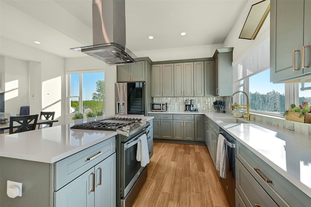 kitchen with sink, island range hood, light hardwood / wood-style floors, stainless steel appliances, and decorative backsplash