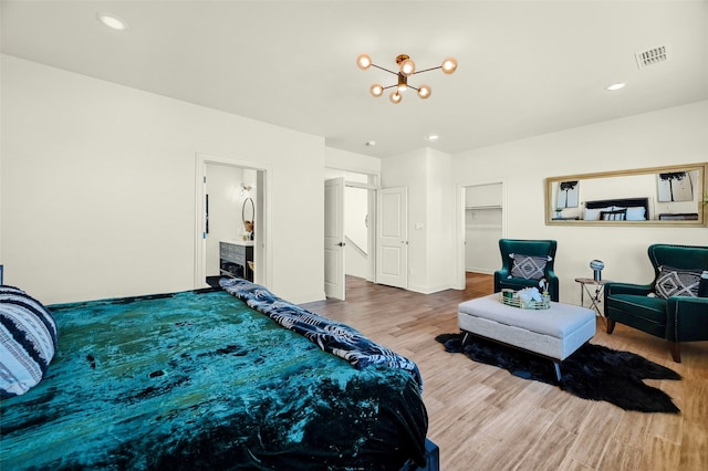 bedroom with a spacious closet, hardwood / wood-style flooring, a closet, connected bathroom, and a notable chandelier