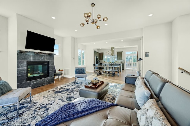 living room with an inviting chandelier, a healthy amount of sunlight, a tiled fireplace, and wood-type flooring