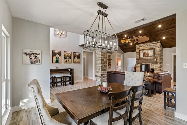 dining space with a fireplace, ornate columns, an inviting chandelier, lofted ceiling, and light hardwood / wood-style flooring