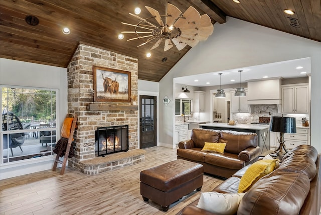 living room with a stone fireplace, wood ceiling, sink, high vaulted ceiling, and light wood-type flooring