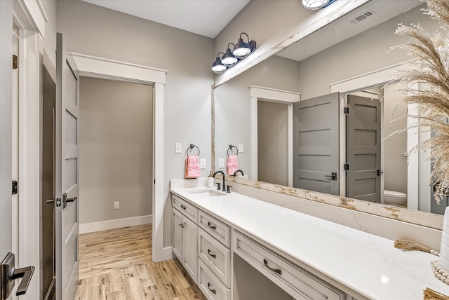 bathroom with toilet, vanity, and wood-type flooring