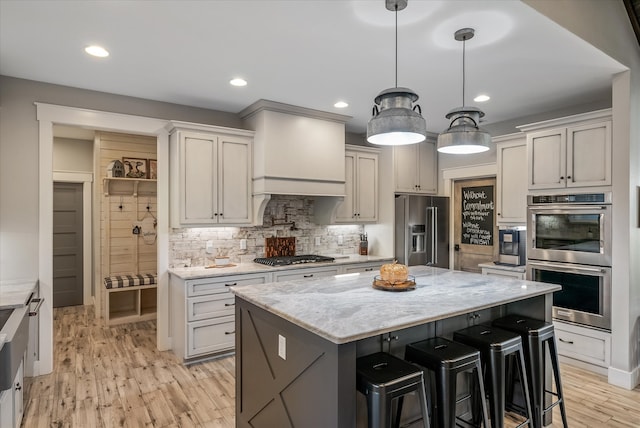 kitchen with light hardwood / wood-style floors, a kitchen island, appliances with stainless steel finishes, and decorative light fixtures