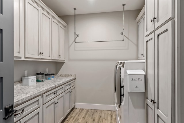 clothes washing area with light hardwood / wood-style flooring, cabinets, and washer and dryer