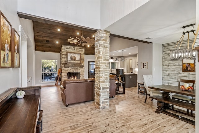 living room featuring high vaulted ceiling, a stone fireplace, a chandelier, light hardwood / wood-style flooring, and decorative columns