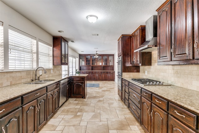 kitchen with appliances with stainless steel finishes, wall chimney exhaust hood, light stone counters, and sink