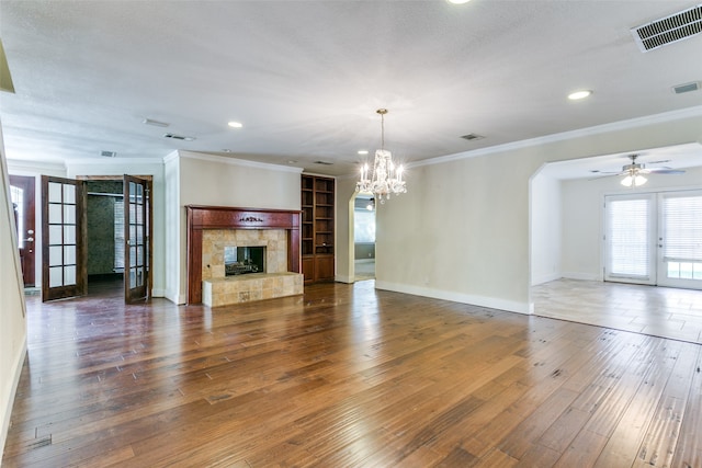 unfurnished living room featuring dark wood-type flooring, crown molding, ceiling fan with notable chandelier, and a tile fireplace