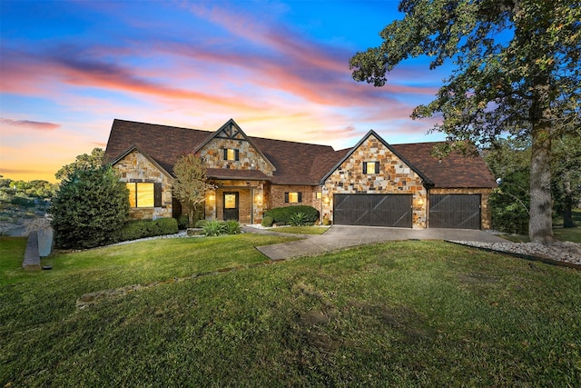 tudor house with a yard, an attached garage, stone siding, and driveway