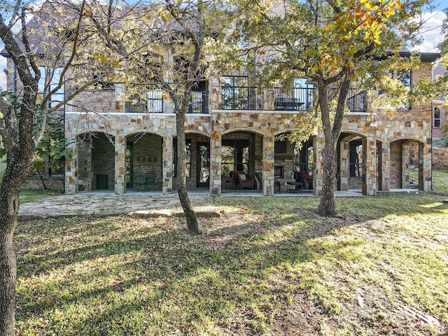 view of front of home featuring stone siding, a patio, a front lawn, and a balcony