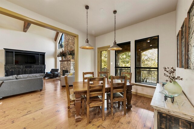 dining space with baseboards, a stone fireplace, vaulted ceiling, and hardwood / wood-style flooring