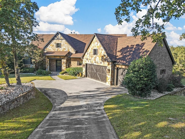 english style home featuring concrete driveway, a shingled roof, stone siding, and a front yard