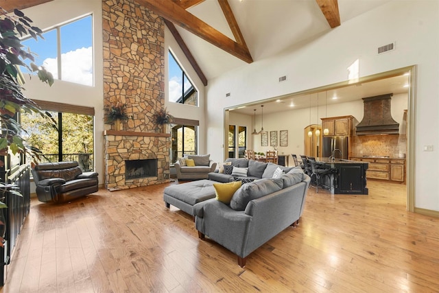 living room with light wood finished floors, visible vents, high vaulted ceiling, beamed ceiling, and a fireplace