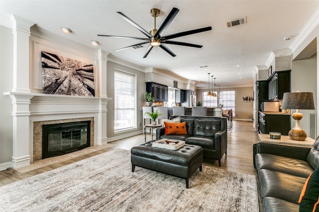 living room with ceiling fan, ornamental molding, a tile fireplace, and light hardwood / wood-style flooring