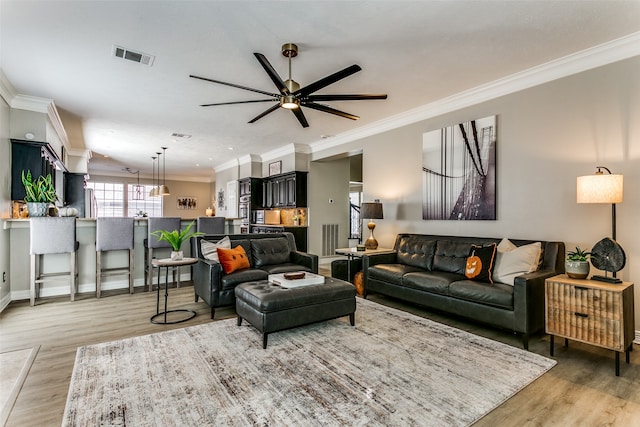 living room featuring ceiling fan, ornamental molding, and light wood-type flooring