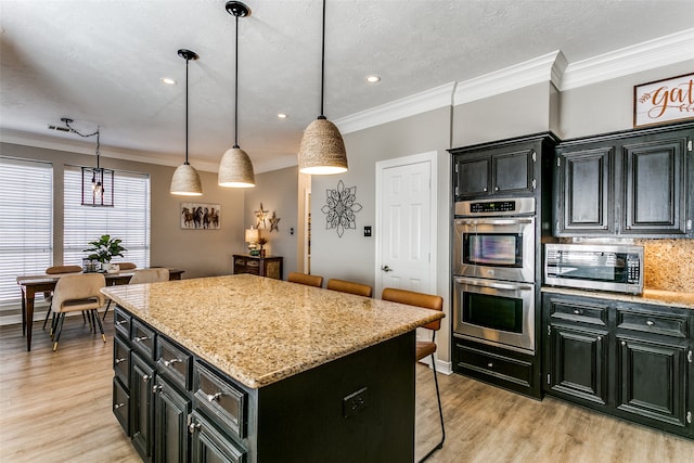 kitchen with a center island, light stone countertops, appliances with stainless steel finishes, decorative light fixtures, and a kitchen bar