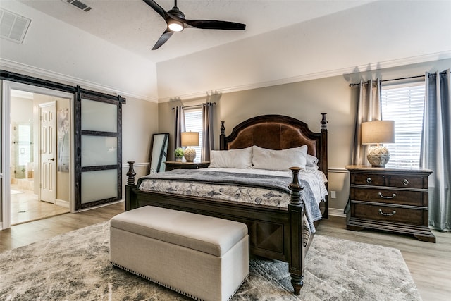 bedroom with ensuite bathroom, ceiling fan, a barn door, light wood-type flooring, and multiple windows