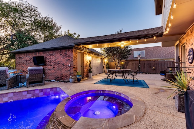 pool at dusk featuring an in ground hot tub and a patio