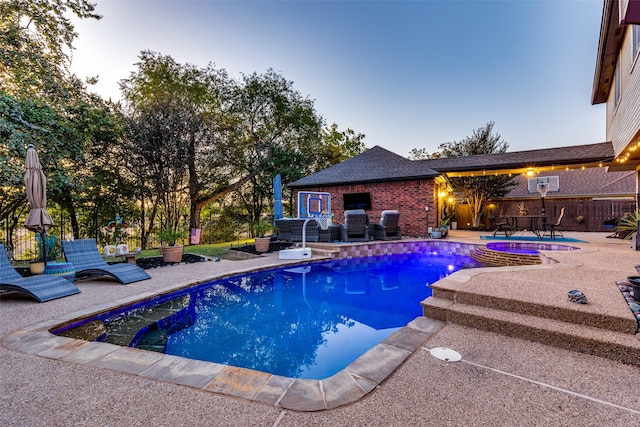 pool at dusk with an in ground hot tub and a patio