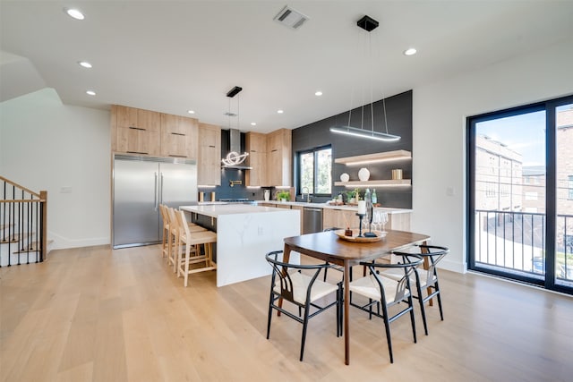 kitchen featuring a kitchen breakfast bar, hanging light fixtures, a center island, appliances with stainless steel finishes, and light hardwood / wood-style floors