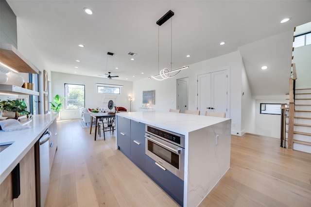 kitchen featuring appliances with stainless steel finishes, a kitchen island, hanging light fixtures, ceiling fan, and light hardwood / wood-style floors