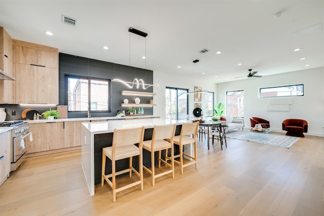 kitchen featuring light brown cabinets, high end stainless steel range oven, a center island, decorative light fixtures, and light hardwood / wood-style floors