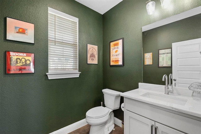 half bathroom featuring toilet, a textured wall, vanity, and baseboards