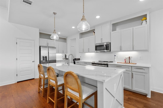 kitchen with dark hardwood / wood-style flooring, appliances with stainless steel finishes, a kitchen island with sink, pendant lighting, and sink