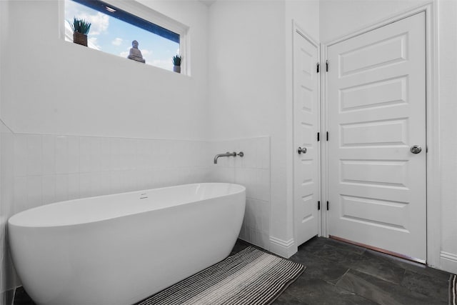 full bathroom with tile walls, a freestanding tub, and wainscoting