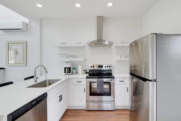 kitchen featuring wall chimney range hood, sink, white cabinetry, stainless steel appliances, and light hardwood / wood-style flooring