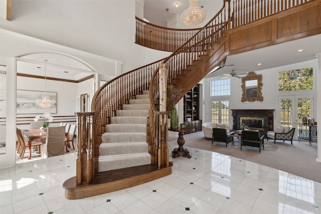 stairs with tile patterned floors, ceiling fan with notable chandelier, a towering ceiling, and crown molding