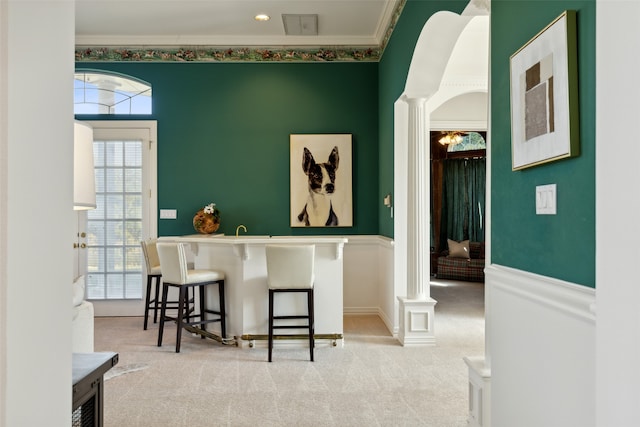 bar featuring light colored carpet, ornamental molding, and ornate columns