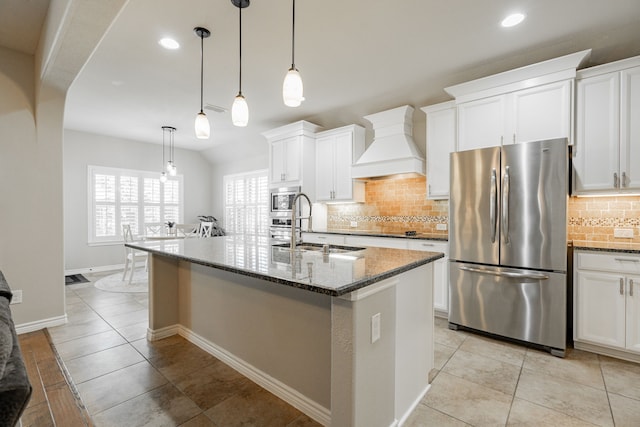 kitchen with a kitchen island with sink, stainless steel appliances, dark stone countertops, custom exhaust hood, and white cabinetry