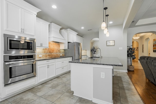 kitchen featuring a kitchen island with sink, light hardwood / wood-style flooring, sink, premium range hood, and appliances with stainless steel finishes