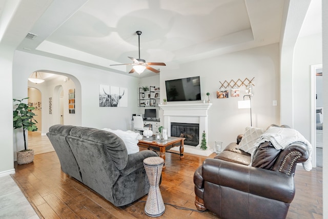 living room featuring wood-type flooring, a tray ceiling, and ceiling fan