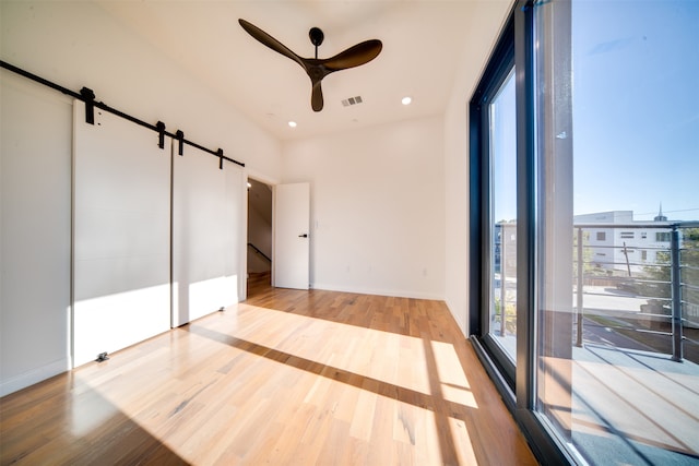 unfurnished bedroom featuring a barn door, light wood-type flooring, and ceiling fan