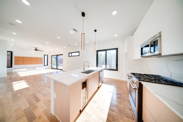 kitchen featuring decorative backsplash, a kitchen island with sink, sink, decorative light fixtures, and appliances with stainless steel finishes