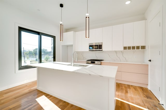 kitchen with light hardwood / wood-style flooring, stainless steel appliances, a center island with sink, decorative light fixtures, and white cabinetry