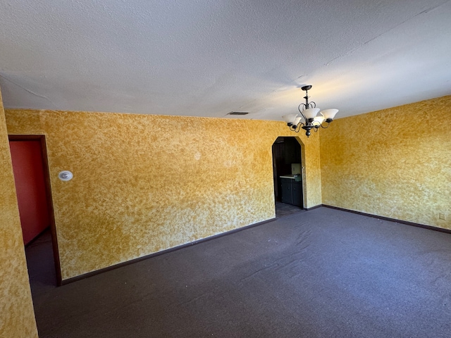 unfurnished room with a notable chandelier, a textured ceiling, and dark carpet