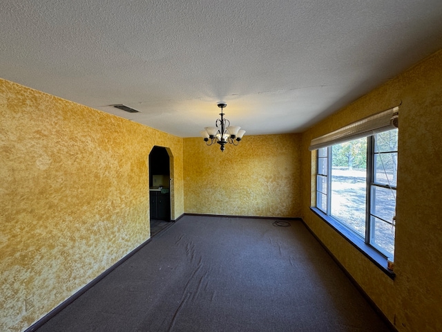 spare room featuring a notable chandelier, a textured ceiling, and dark carpet