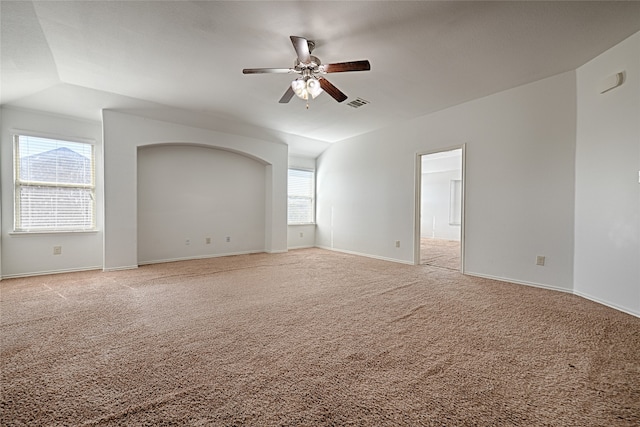 empty room with a wealth of natural light, vaulted ceiling, light colored carpet, and ceiling fan